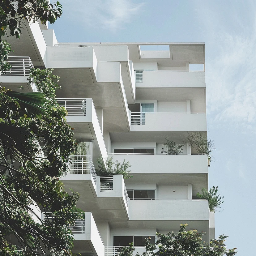 Edificio blanco de departamentos con balcones y vegetación contra un cielo azul: comprar la primera vivienda
